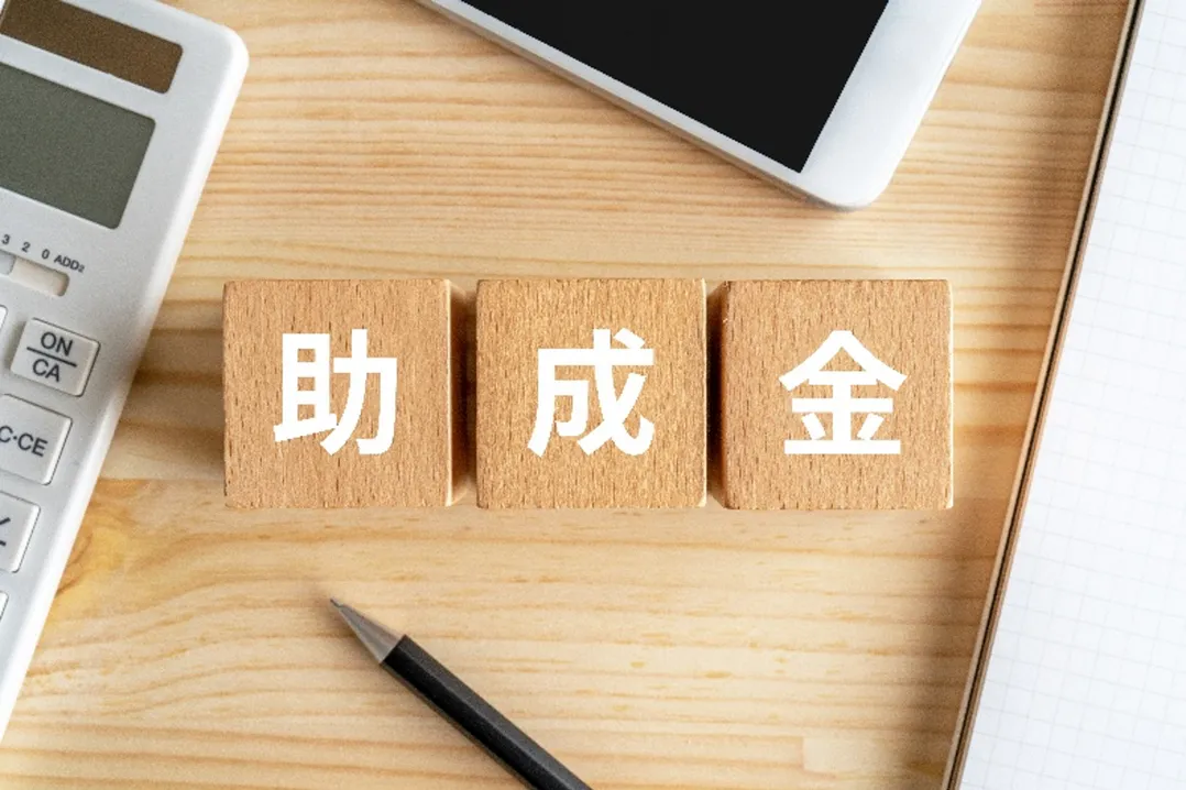 助成金申請や処遇改善の取り組みを連想させる「助成金」の木製ブロックと電卓・ノートの画像