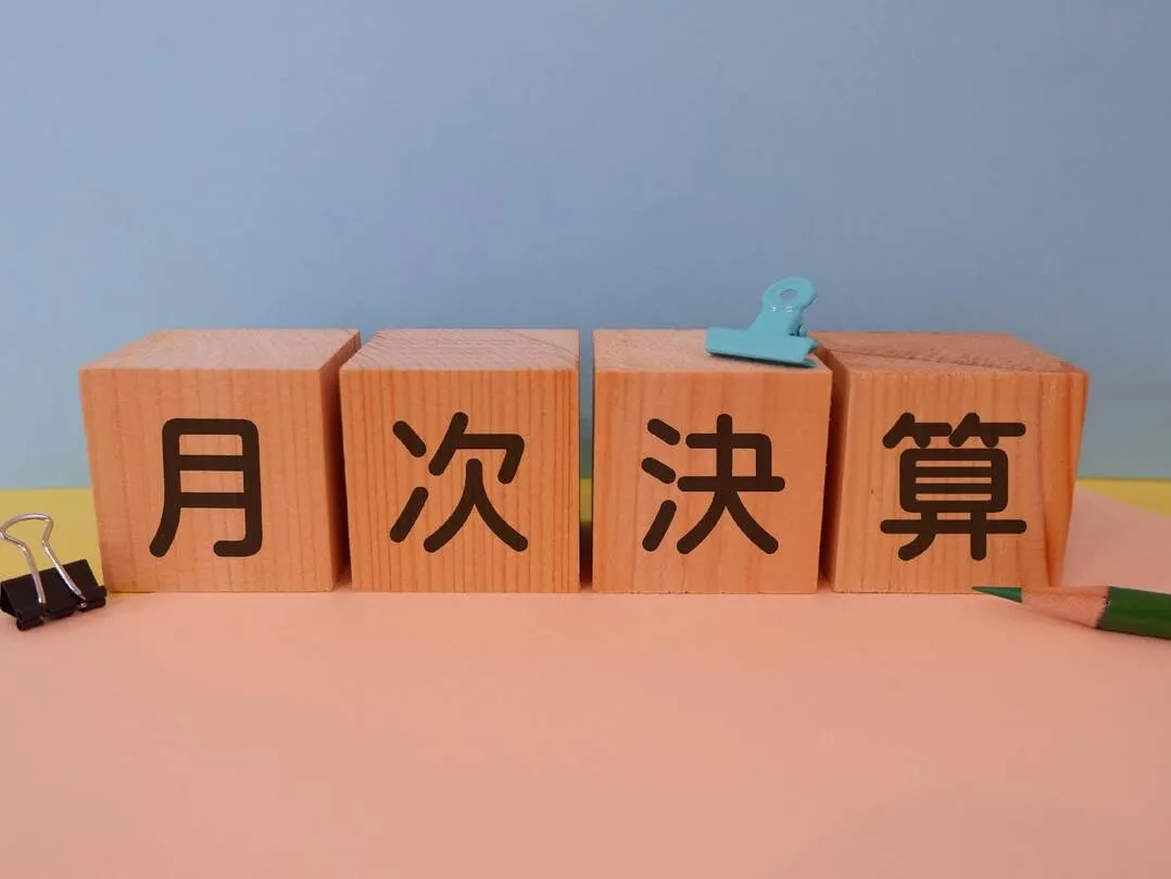 月次決算の文字が書かれた木製ブロックと文房具、定期的な会計監査を象徴するイメージ
