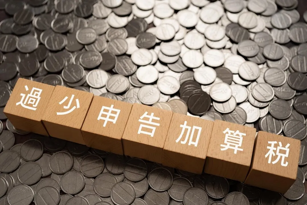 過少申告加算税を表す木製ブロックと硬貨、税負担のイメージ