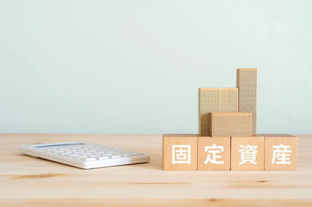 固定資産を象徴する木製ブロックと電卓、修繕費と資本的支出の判断に関連