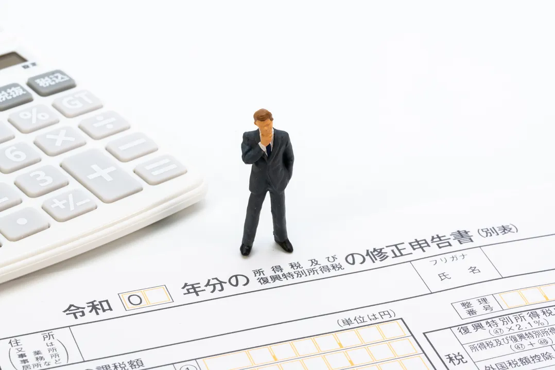 附帯税の申告を連想させる税務書類と電卓、スーツ姿のフィギュア